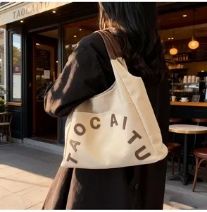 Canvas tote bag detail view showing brown leather shoulder straps and stylish letter embroidery.