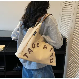 Detail view of large canvas tote bag with brown leather handles and chic letter embroidery.
