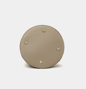 Taupe bucket bag bottom detail featuring premium pebbled leather and gold protective metal feet.