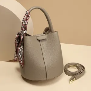 Stylish taupe leather bucket bag with top handle, chic twilly scarf, and versatile crossbody strap.