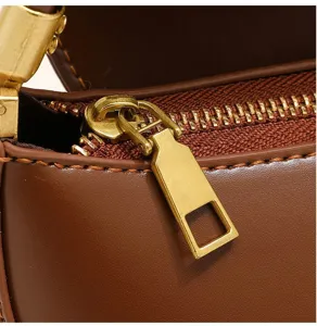 Close-up detail of brown leather bag zipper and golden metal hardware with fine stitching.