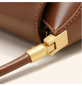 Close-up detail of brown leather handbag featuring gold-tone metal hardware and fine stitching.