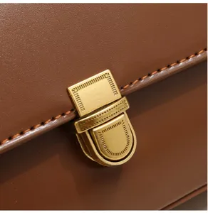 Close-up detail of stylish brown leather shoulder bag with vintage metal lock and fine stitching.