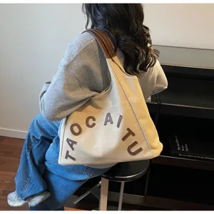 Spacious beige canvas tote bag with brown leather handles and chic letter embroidery for commute.
