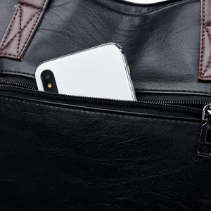Close-up detail of black soft leather handbag showing front zipper pocket and phone.