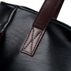 Close-up detail of the black soft leather handbag showing reinforced brown strap stitching.