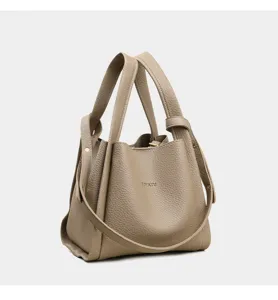 Vista detallada del elegante bolso cubo de cuero taupe con asas dobles y correa ajustable.
