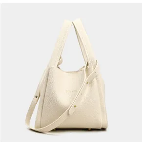 Vista detallada del bolso tipo cubo de cuero beige con textura granulada y herrajes.