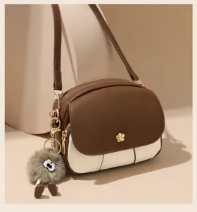 Close-up of stylish brown and white color-block crossbody bag detail with cute plush doll pendant.