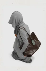 Close-up detail shot of a large brown soft leather tote bag featuring slim straps and tag.