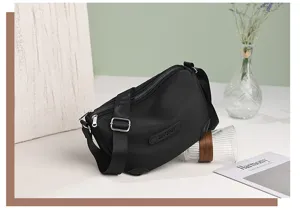 Black nylon crossbody bag detail, featuring multi-zipper pockets and adjustable strap.