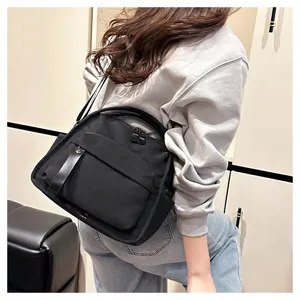Detail view of black commuter crossbody bag, showing nylon fabric, dual zippers and front pocket.