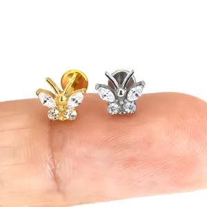 Gedetailleerde close-up van vlinder piercing oorknopjes met zirkonia op vinger voor schaal.