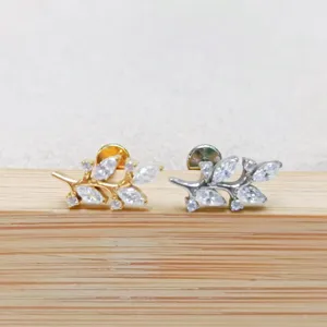 Dettaglio di gioiello piercing ramo foglia in acciaio titanio, oro e argento.