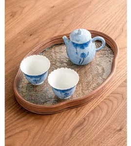 Detailed shot of hand-painted blue lotus ceramic teapot and two tea cups on decorative wooden tray.