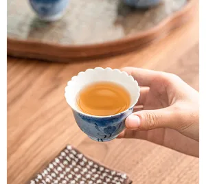 Close-up of hand-painted ceramic tea cup detail showing lotus design and warm tea.