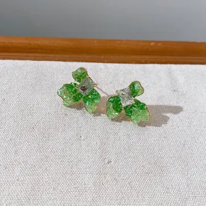 Detail close-up shot of gradient green crystal flower bow earrings, sparkling stone detail.