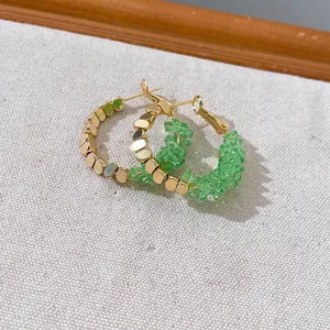 Close-up detail of stylish green crystal chip and gold disc hoop earrings, elegant jewelry.