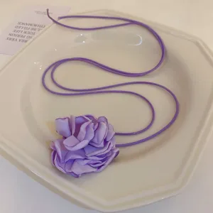 Gros plan détaillé d'un collier de fleurs en tissu violet sur une assiette en céramique blanche.