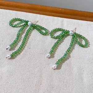 Detailed close-up view of elegant green crystal beaded bow earrings with pearl details.