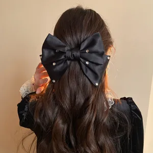 Detail shot of elegant black satin bow hair clip with sparkling rhinestones for chic styling.