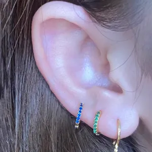 Primo piano di orecchini a cerchio cartilagine con zirconi colorati, dettaglio piercing.