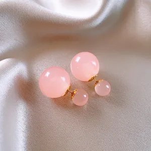 Primo piano dettaglio degli orecchini a lobo con doppia sfera in vetro rosa dorato fine.