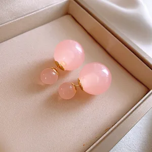 Primo piano di orecchini a sfera rosa a doppia faccia con spilli dorati, dettaglio in scatola.