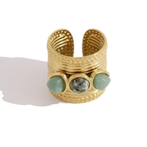 Close-up of wide gold-colored open ring featuring three bezel-set green natural stones.