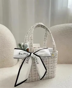 Nahaufnahme der eleganten Tweed-Handtasche mit stilvoller schwarz eingefasster weisser Schleife.