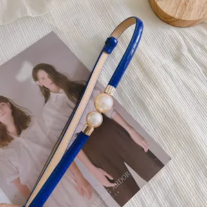 Détail de fine ceinture bleue avec élégante boucle double perle métal sur beau tissu.