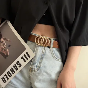Detail shot of a brown leather belt featuring interlocking gold rings worn with jeans.