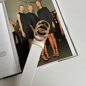 Close-up detail of white fashion leather belt featuring three interlocking gold rings.