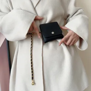 Close-up detail of a chic black mini pouch with woven gold leather chain belt fashion accessory.