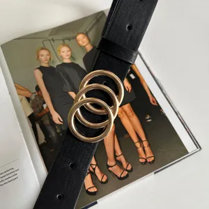 Close up detail of women black leather belt with creative gold triple ring buckle for jeans.