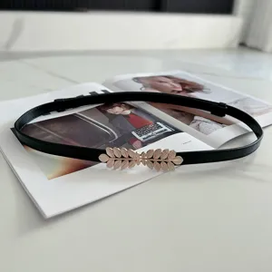Close-up detail of a black thin belt featuring an elegant gold leaf buckle and adjustable fit.