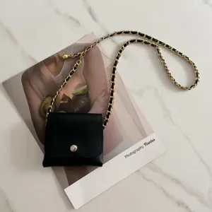Detail shot of black mini waist bag featuring woven chain strap on aesthetic magazine prop.