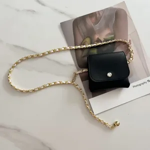Detail shot of stylish black mini waist bag with gold woven chain belt, trendy accessory.