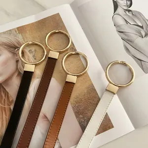 Detailed view of women's thin leather belt with gold round ring buckle, versatile dress accessory.