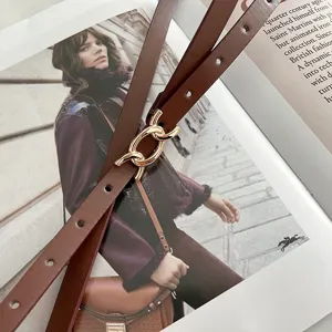 Dettagli in primo piano della sottile cintura in pelle marrone da donna con fibbia in metallo dorato.