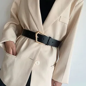 Detail van de zwarte lederen riem met gouden gesp gedragen over een chique beige blazer