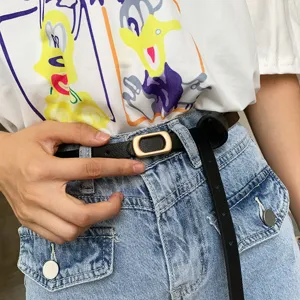 Minimalist black thin leather belt detail, featuring a sleek gold rectangular metal buckle.