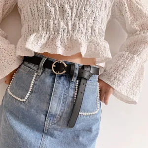 Close-up detail of women's black leather belt with gold round buckle worn with denim skirt.