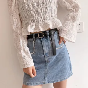 Stylish black leather belt with metal round buckle, paired with casual denim skirt for women.