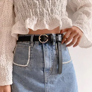 Close-up view of a minimalist black leather belt with a metal round buckle worn on jeans.