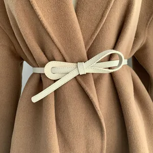 Vue détaillée d'une élégante ceinture fine blanche en cuir portée sur un manteau.