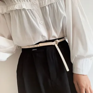 Primo piano di una cintura sottile beige minimalista con fibbia quadrata di metallo e pantaloni.