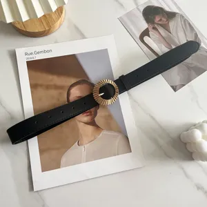 Detailansicht des schwarzen Damengürtels mit goldener runder Schnalle auf Marmor.