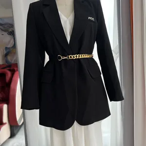 Ceinture chaîne métal femme assortie au blazer noir et robe blanche, détail élégant.