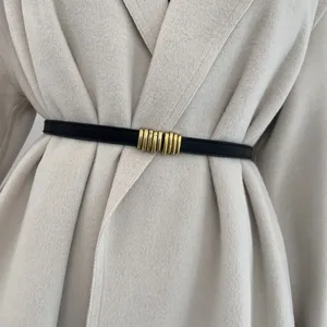 Primo piano di sottile cintura nera da donna con fibbia dorata vintage indossata sul cappotto.
